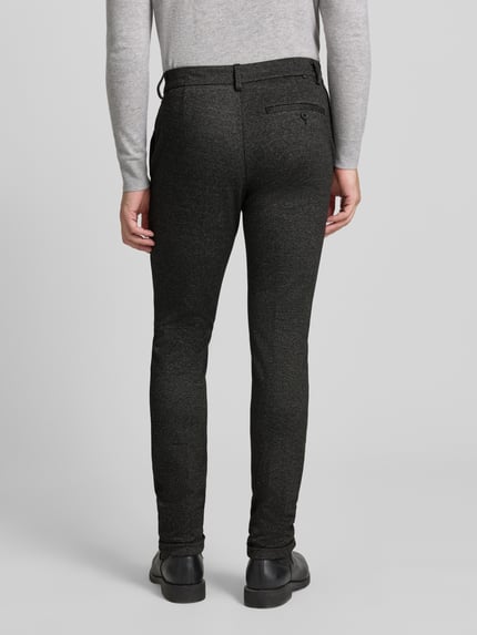 Männermodel trägt Slim Fit Chino mit Viskose-Anteil van Tom Tailor Denim, allover-motief, zijzakken, detailopname geheel van achteren.