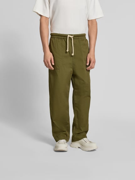 Mężczyzna nosi Balloon Fit Stoffhose aus Baumwolle od Officine Générale, jasnokhaki, bawełniany canvas, kieszenie, elastyczny pas ze sznurkiem, Szerokość w rozmiarze 50: 41 cm, długość nogawki 71 cm, Ganzkörperansicht von vorne.