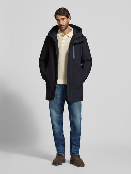 Männermodel trägt Regular Fit Parka mit Stehkragen Modell 'FLEX CROSS PARKA' von Strellson in Dunkelblau, Jeans und braunen Schuhen, Ganzkörperansicht von vorne. Herren Parka von Strellson.