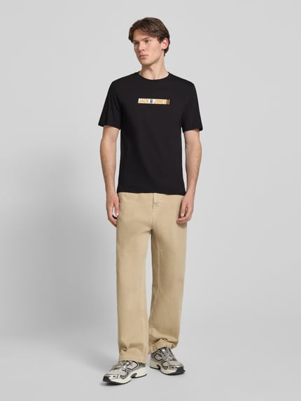 Männermodel trägt Regular Fit T-Shirt mit Logo-Print Modell 'Munk' von JACK & JONES aus Reiner Baumwolle, schwarzer Stoff, Rückenlänge bei Größe M: 74 cm, Ganzkörperansicht von vorne.