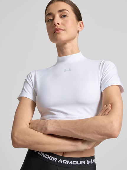 Vrouwenmodel draagt Cropped T-Shirt met Logo en Stehkragen van Under Armour, wit, materiaalmix met stretch, ruglengte maat S 30 cm, Nahaufnahme Oberkörper.