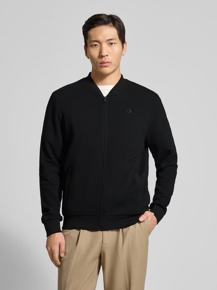 Męski model nosi Regular Fit Sweatjacke aus reiner Baumwolle von Drykorn, czarna, gładka, z zamkiem, logo-patch, college'owy kołnierz, rękawy długie, ściągacze, bawełna. Ganzkörperansicht von vorne.