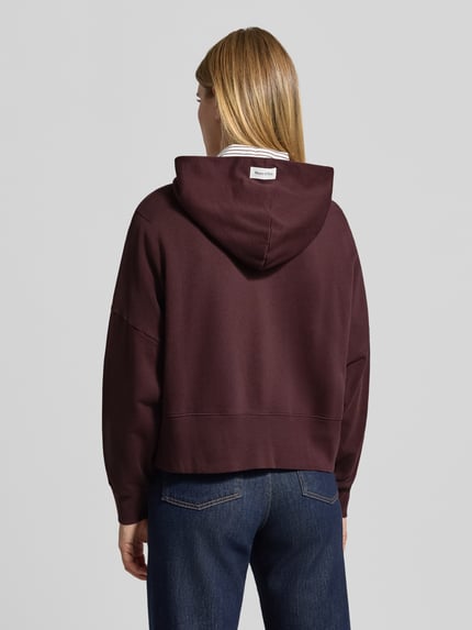 Frauenmodel trägt Sweatshirt mit Kapuze und Label-Detail von MARC O'POLO in Dunkelrot, Jersey, unifarben, Ganzkörperansicht Rückansicht.