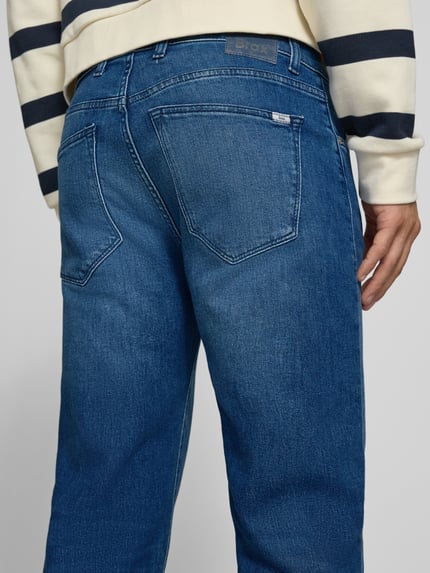 Männermodel trägt Relaxed Fit Jeans aus Baumwoll-Mix Modell 'Clint' von Brax, blaue Jeans, dezente Waschung, Herren Wide & Loose Fit Jeans, Ganzkörperansicht Rückansicht.