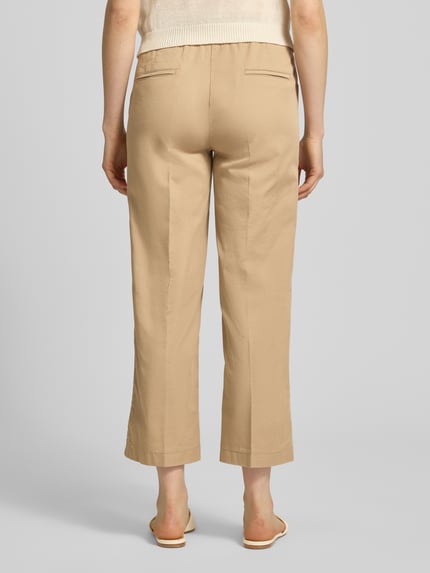 Vrouwenmodel draagt Wide Fit stoffen broek in 7/8-lengte model 'Sue' van TONI in beige katoenmix met persplooien, steekzakken, elastische band met tunnelkoord, binnenbeenlengte 66 cm bij maat 36, bandwijdte 34 cm, geheelopname achteraan