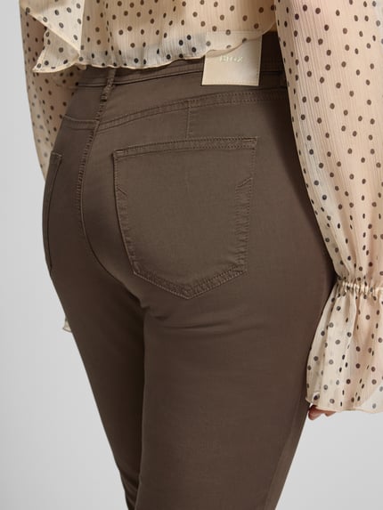 Frauenmodel trägt Hose in verkürzter Passform Modell 'Mary' von Brax aus Baumwoll-Lyocell-Mix mit Eingrifftaschen, Detailaufnahme Rückansicht.
