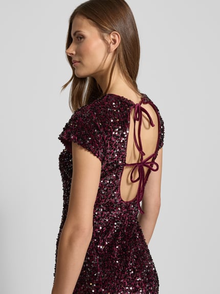 Frauenmodel trägt Minikleid mit Pailletten Modell 'XWILL' von Mango, samtig, figurnah, burgunderrot, rückseitige Schnürung, Detailaufnahme Rückansicht.
