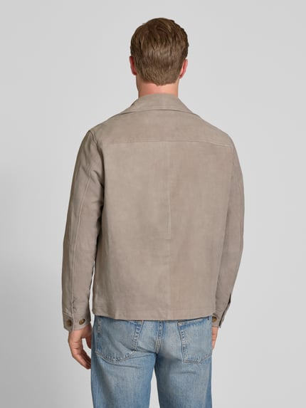 Męski model nosi Regular Fit Lederjacke aus echtem Ziegenvelours Modell 'THOM' von SELECTED HOMME w jednolitym kolorze, krój regular fit, kołnierz wykładany, długie rękawy z mankietami, kieszeń na piersi, kieszenie boczne, kieszeń wewnętrzna, wykonana z prawdziwej skóry koziej, tekstura zamszowa, widok całej sylwetki z tyłu.