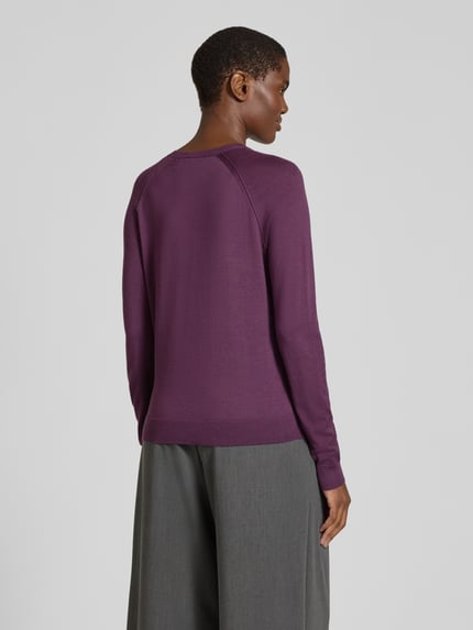 Frauenmodel trägt Strickjacke aus Wolle mit Raglanärmeln von BOSS in Uni-Lila mit Rundhalsausschnitt, Feinstricktextur, Ganzkörperansicht Rückansicht.