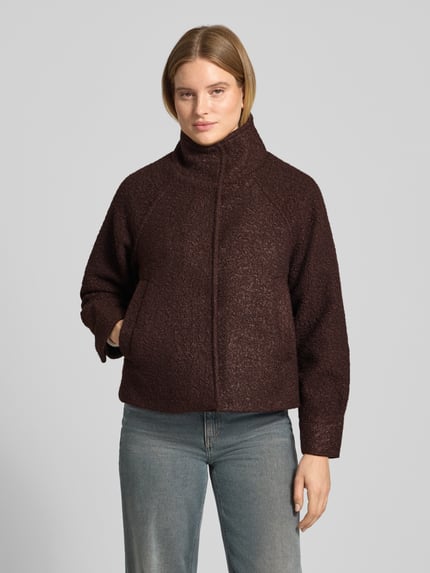 Frauenmodel trägt Kurzmantel mit Stehkragen Modell 'SC-GISA 1' von SOYACONCEPT in Dunkelbraun, strukturierte Bouclé-Oberfläche, unifarben, verdeckter Reißverschluss und Knopfleiste, Langarm mit Raglanärmeln, Ganzkörperansicht von vorne.