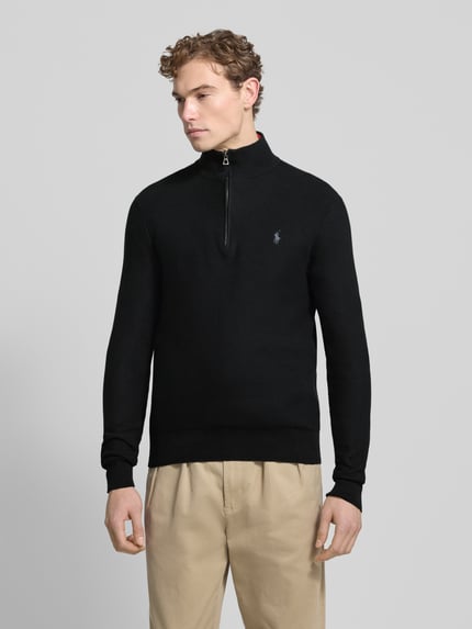 Męski model nosi Sweter z dzianiny z wyhaftowanym logo od Polo Ralph Lauren, bawełna, krój regular fit, prążkowane wykończenia, stójka, krótki zamek błyskawiczny, długość tyłu 70 cm, długość rękawa 68 cm, kolor czarny, faktura gładka, widok całościowy z przodu.