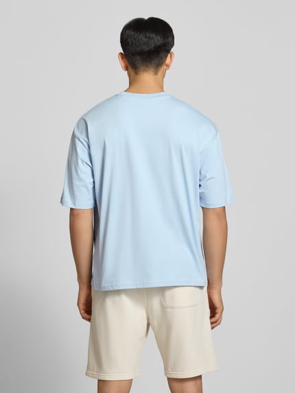 Männermodel trägt T-Shirt mit Logo- und Motiv-Print von REVIEW, hellblau, Loose-Fit, Reine Baumwolle, Rückenlänge 70 cm, Ganzkörperansicht Rückansicht.