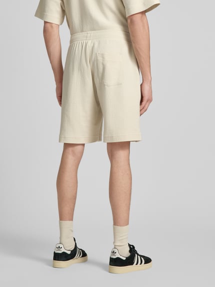 Männermodel trägt Shorts mit Label-Stitching von REVIEW aus Baumwoll-Mix, Regular-Fit, Strukturmuster, Farbe Creme, Ganzkörperansicht Rückansicht.