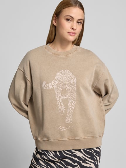 Kobiece modelka nosi Oversized Sweatshirt mit Motiv-Print von Lala Berlin, bawełna, krój oversized fit, nadruk z motywem, okrągły dekolt, elastyczne wykończenia, długość tyłu w rozmiarze S: 56 cm, beżowe odcienie, Ganzkörperansicht von vorne.