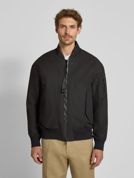 Męski model nosi Regular Fit Jacke aus Baumwoll-Mix Modell 'Pulse' von g-lab, mieszanka bawełny, krój regular fit, stójka, Kieszeń na rękawie, wpuszczane kieszenie, elastyczne wykończenia, Długość tyłu w rozmiarze M: 70 cm, Szerokość ramion w rozmiarze M: 55 cm, Szerokość klatki piersiowej w rozmiarze M: 50 cm, Długość rękawów w rozmiarze M: 61 cm, kolor czarny, matowa tekstura, widok całej sylwetki z przodu.