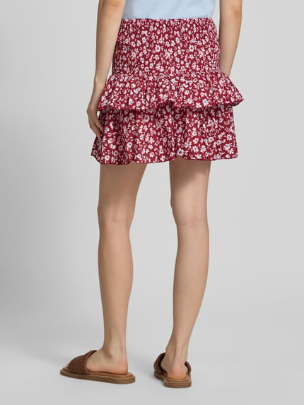 Vrouwenmodel draagt uitlopend dames minirok met all-over bloemenmotief, volantdetails, gesmokte boord, puur katoen, model 'ZOEY' van Only. Ganzlichaamsweergave achteraan.