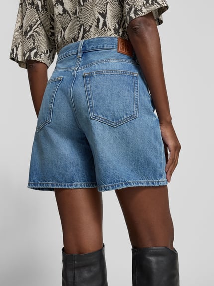 Frauenmodel trägt Jeansshorts aus reiner Baumwolle von Anine Bing in A-Linie mit 5-Pocket-Design und Kontrastnähten, Ganzkörperansicht Rückansicht.