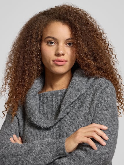 Kobiece model nosi szary Regular Fit Strickpullover mit Woll-Anteil Modell 'SHINE' od Only o melanżowej fakturze, długi rękaw, prążkowane wykończenia, dzianina, dekolt carmen, zbliżenie na górną część ciała.