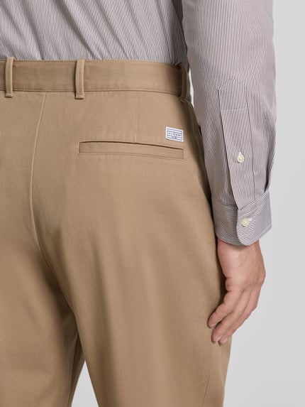 Männermodel trägt Wide Fit Bundfaltenhose aus reiner Baumwolle von Tommy Hilfiger in Beige mit Label Stitching, Nahaufnahme Rückansicht.