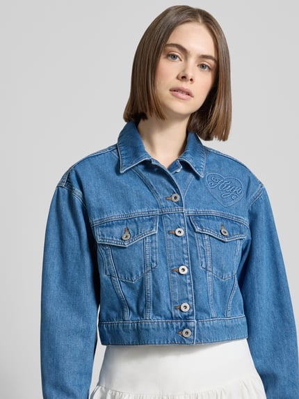 Vrouwenmodel draagt Regular Fit jeansjack katoenmix model 'GALATEA_B' van Hugo Blue in denimlook met labelapplicatie, korte lengte, lange mouw, platte kraag, knoopsluiting en klepzakken, materiaal: katoenmix, voorkant bovenlichaam close-up.