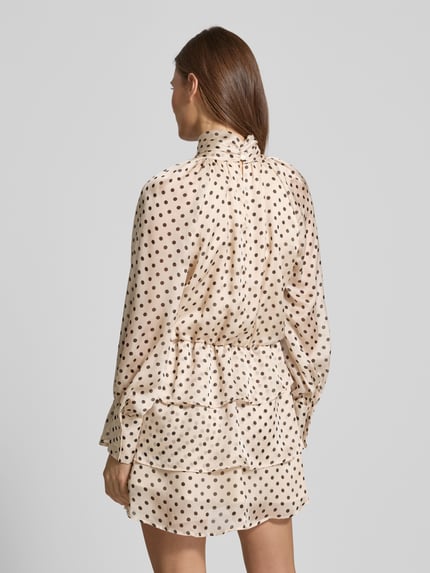 Frauenmodel trägt Cocktailkleid im Stufen-Look mit Stehkragen von Rinascimento, cremefarben mit braunen Punkten, Satin, taillierter Schnitt, Minikleid, Ganzkörperansicht Rückansicht.