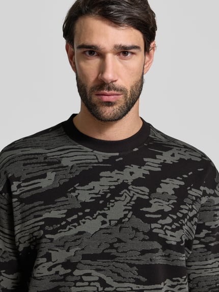 Mężczyzna nosi Regular Fit T-Shirt aus reiner Baumwolle Modell 'TE_WILDNATURE' von BOSS Orange w abstrakcyjny wzór, okrągły dekolt, krótki rękaw, feinstrick, label patch, optyka allover, materiał: czysta bawełna, kontekst: Herren T-Shirt, Nahaufnahme górnej części ciała.