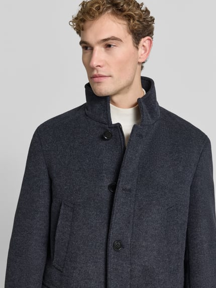 Mannelijk model draagt Regular Fit Mantel mit Stehkragen van Christian Berg Men, wolmix, knoopsluiting, klepzakken, detailopname bovenlichaam.