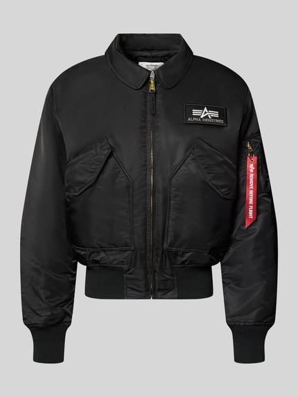 Produktfoto, schwarze Bomberjacke mit seitlichen Pattentaschen und Label-Patch von Alpha Industries, glatte Oberfläche, goldfarbener Reißverschluss, Rippenbündchen, Kentkragen, Regular Fit, Reißverschlusstasche am Ärmel mit Label-Detail, minimalistisches Design, Produktname: Bomberjacke mit seitlichen Pattentaschen und Label-Patch von Alpha Industries, Rückenlänge 62 cm, Schulterbreite 50 cm, Brustweite 61 cm, Ärmellänge 67 cm