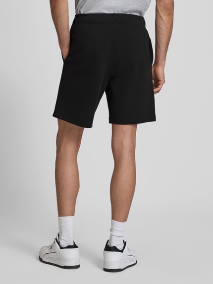 Männermodel trägt schwarze Shorts mit elastischem Bund und Label-Stitching von CHAMPION, Baumwoll-Mix, Ganzkörperansicht Rückansicht.