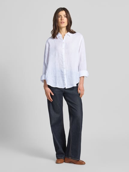 Vrouwenmodel draagt overhemdblouse uit zuiver linnen met kentkraag model 'MIRA' van 0039 Italy, regular fit, knoopsluiting, sportmanchet, ruglengte 68 cm, mouwlengte 62 cm, witte kleur, rechte vormen, gladde textuur, volledige lichaamsvoorzijde.