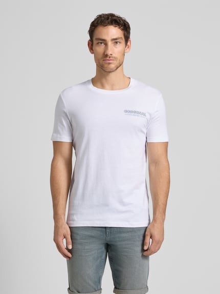 Męski model nosi Regular Fit T-Shirt aus reiner Baumwolle von Tom Tailor Denim, kolor biały, krótki rękaw, nadruk logo, widok z przodu, ujęcie całej sylwetki.