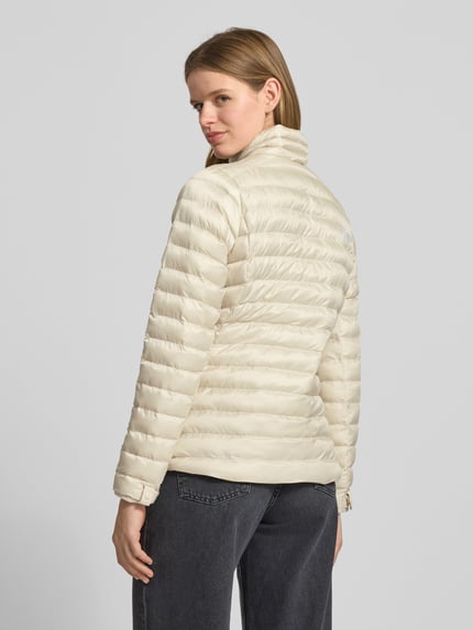 Frauenmodel trägt Steppjacke mit Stehkragen und Label-Stitching von The North Face in Beige, gesteppt, Regular Fit, Rückansicht, Ganzkörperansicht. Reißverschluss, Reißverschlusstaschen, Rückenlänge 62 cm, Schulterbreite 38 cm, Brustweite 46 cm, Ärmellänge 64 cm.