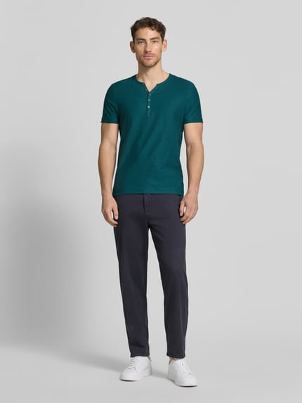 Męski model nosi T-Shirt mit V-Ausschnitt und Knopfleiste od MCNEAL, czysta bawełna, krój regular fit, długość tyłu w rozmiarze M: 68 cm, całopostaciowy widok z przodu