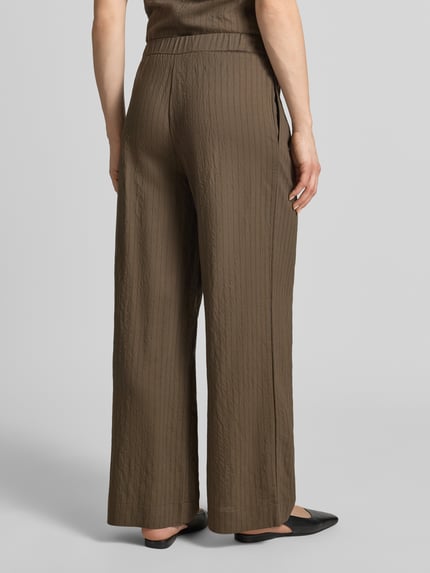 Frauenmodel trägt Stoffhose aus Viskose-Mix Modell 'TATU' von Mango, braun, Wide Leg, elastischer Bund, strukturierte Oberfläche, Ganzkörperansicht Rückansicht.