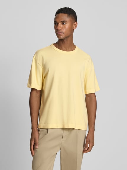 Männermodel trägt Cropped T-Shirt mit Rundhalsausschnitt von GAP in Gelb, reine Baumwolle, lockerer Schnitt, Ganzkörperansicht von vorne.