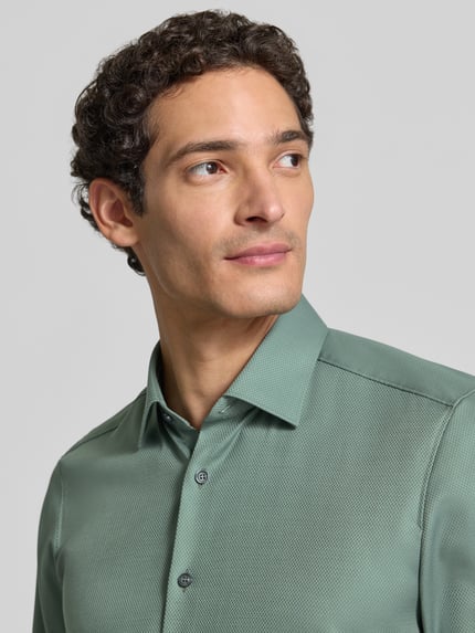 Männermodel trägt Slim Fit Businesshemd mit Kentkragen von OLYMP in Grün, feine Struktur, Knopfleiste, Nahaufnahme Oberkörper.