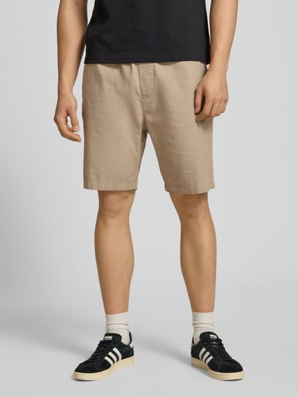 Mężczyzna nosi Straight Fit Shorts mit Gesäßtasche od REVIEW w beżowym kolorze, z lnu, kieszeń z tyłu, elastyczny pas, szerokość w rozmiarze M 44 cm, długość nogawki 21 cm, widok całej sylwetki z przodu.