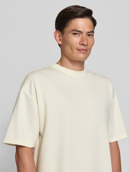 Männermodel trägt Oversized T-Shirt mit überschnittenen Schultern von REVIEW x ANSONÂ´S in Creme, glatte Struktur, Nahaufnahme Oberkörper.