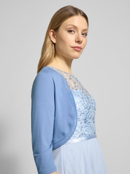 Modelka nosi Bolero aus Viskose-Mix mit 3/4-Arm od V.M., jasnoniebieski kolor, dopasowany krój, 3/4 rękaw, długość tyłu 36 cm w rozmiarze 36, z przodu zbliżenie górnej części ciała.