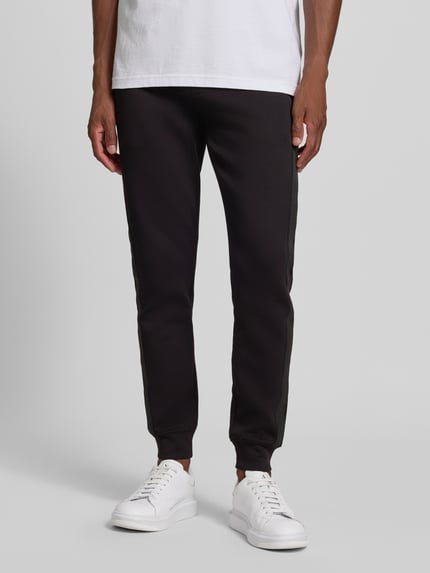 Männermodel trägt Sweatpants mit Bordüre von Armani Exchange in Schwarz, gerader Schnitt, mit Label-Print, Ganzkörperansicht von vorne.