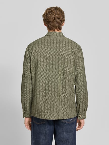 Männermodel trägt Relaxed Fit Hemdjacke mit Kentkragen und Brusttaschen von Scotch & Soda, Allover-Muster, Material-Mix, Ganzkörperansicht Rückansicht.
