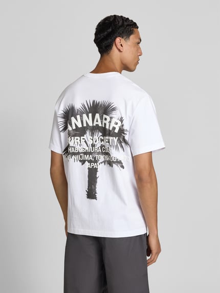 Männermodel trägt Relaxed Fit T-Shirt mit Logo-Print von ANNARR aus Reine Baumwolle, Weiß mit Palmenmotiv, Rückenlänge 72 cm, Ganzkörperansicht Rückansicht.