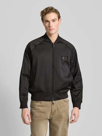 Męski model nosi Bomberjacke mit Reißverschluss od ARMANI EXCHANGE, czarny materiał z bawełną, regular fit, widok całej sylwetki z przodu.