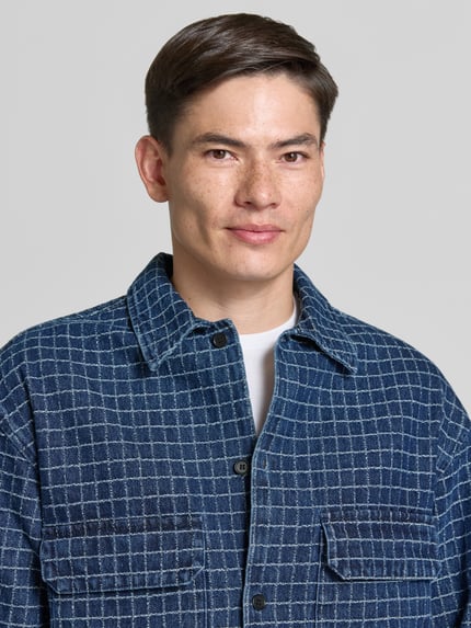Męski model nosi Regular Fit Hemdjacke mit Viskose-Anteil Modell 'David' od Wood Wood, bawełniany miks z domieszką wiskozy, kratka w odcieniach niebieskiego, kołnierz kent, listwa guzikowa, kieszenie na piersi, kontekst: długość tyłu w rozmiarze M: 74 cm, ujęcie: zbliżenie górnej części ciała.