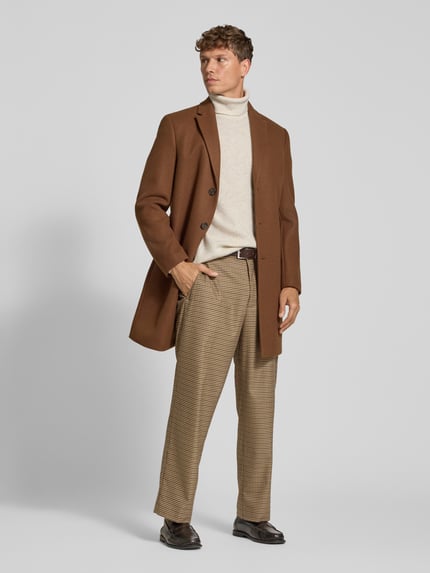 Männermodel trägt Strickpullover in Ripp-Optik mit Rollkragen von Lindbergh in Beige, kombiniert mit braunem Mantel, Ganzkörperansicht von vorne. Rückenlänge bei Größe M 74 cm, Ärmellänge 62 cm, Regular Fit.