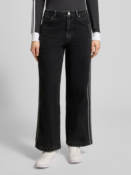 Frauenmodel trägt Loose Fit Jeans aus reiner Baumwolle von adidas Originals in Schwarz mit Kontraststreifen, 5-Pocket-Design, Ganzkörperansicht von vorne.