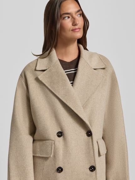Frauenmodel trägt Regular Fit Mantel aus elastischem Baumwoll-Mix Modell 'PICAROL' von MANGO in Beige mit Reverskragen, Nahaufnahme Oberkörper.