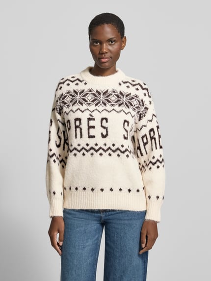 Frauenmodel trägt Pullover mit Ballonärmeln von VERO MODA in Creme mit schwarzem geometrischem Jacquard-Allover-Muster, Strickoptik, Ganzkörperansicht von vorne.