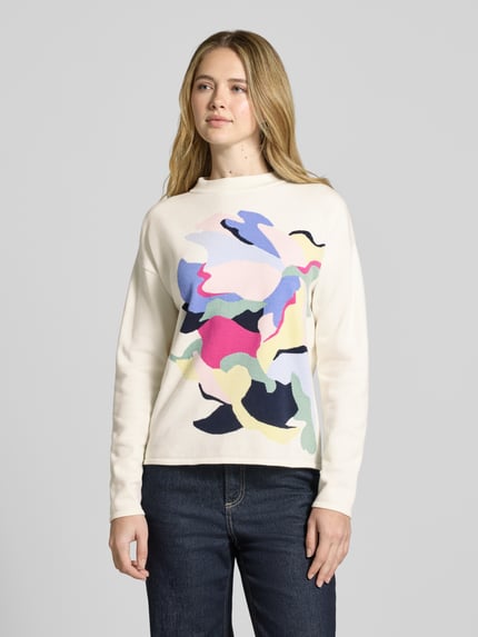 Frauenmodel trägt Strickpullover aus Viskose-Mix mit überschnittenen Schultern von Christian Berg Woman in Relaxed-Fit, Motiv-Design, cremefarbener Grundton mit buntem Muster, Rückenlänge bei Größe S 57 cm, Ärmellänge 57 cm, Ganzkörperansicht von vorne.