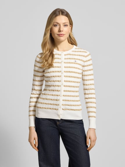 Frauenmodel trägt Strickjacke mit Baumwoll-Anteil von Gant, beige-weiß gestreift, Zopfmuster, Knopfleiste, körpernah, Ganzkörperansicht von vorne.